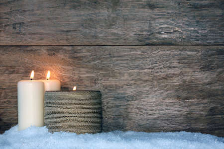 New Year background - burning candles on the snow on a wooden background.の写真素材