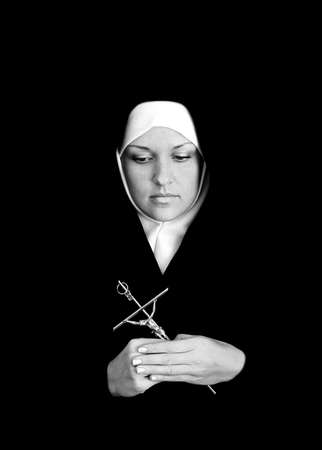 Young catholic nun holding cross in her hands. Photo on black background.の写真素材