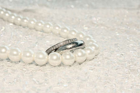 Engagement white gold ring and wedding band with diamonds on a pearl necklaceの写真素材