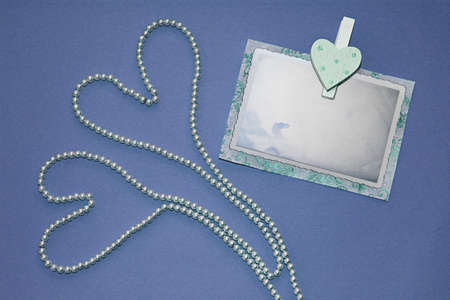 Two hearts of pearl necklaces and pin with old photo frame on blue background. Invitation to your celebration, Wedding card, Valentine's day card, Greeting card.の写真素材