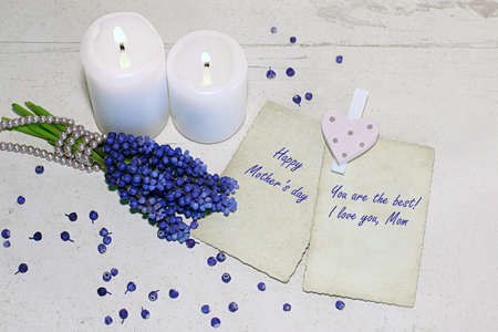 Mother's Day, Women's Day or other suitable holiday card. Background with two white burning candles, fresh blue muscaries bouquet and two old photo frames on vintage wooden planks. With text.の写真素材
