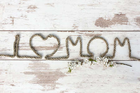 I love Mom. Composition on Mother's Day. Rope text with branches of sakura on the wooden table, closeup.の写真素材