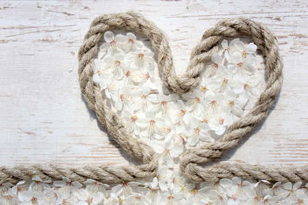 Composition on Mother's Day. Rope heart with flower and blossoms on the wooden table, closeup.の写真素材