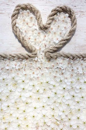 Composition on Mother's Day. Rope heart with flower and blossoms on the wooden table, closeup.の写真素材