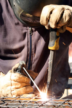 Welder welding  a metal part wearing standard protection equipment