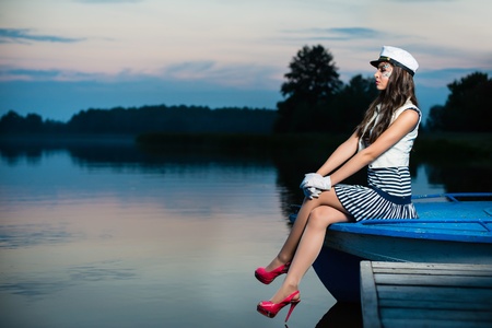 Young beautiful sailor woman sitting on the boat at sunsetの写真素材