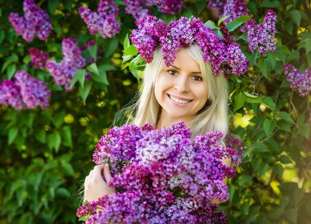 Beautiful smiling young woman is wearing wreath and bouquet of lilac flowersの写真素材