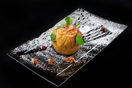 Gourmet Baked Apple. Autumn dessert on black background with sugar, mint, walnutの写真素材