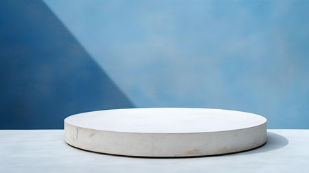 Round stone podium in front of a blue studio background. White Pedestal for Product Presentationの素材