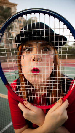Young woman looking through tennis racket