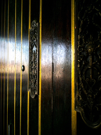An ornate brass decoration on dark brown wooden door. Closeup to brass fittings and golden verticle lineの写真素材