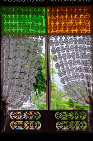 Thai classic wooden and colorful glass window with white knitting curtain and wooden craft.の写真素材