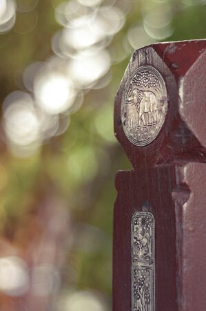 Round Silver metal lamella with elephant stressing embossed on the wooden gate pole. Shallow dept of field. bokeh in background.の写真素材