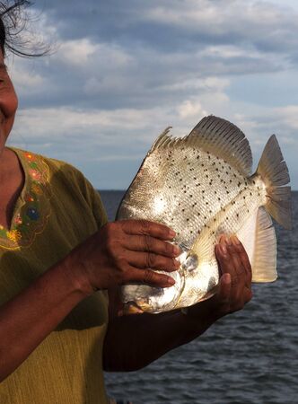 Woman holding a fish on the harbor with the sea and sky behind.の写真素材