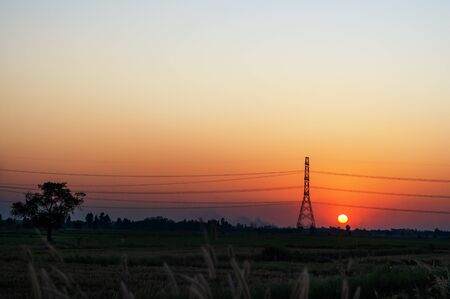 High voltage electric tower and transmission lines across the field when sunset. Electricity pylon.の写真素材
