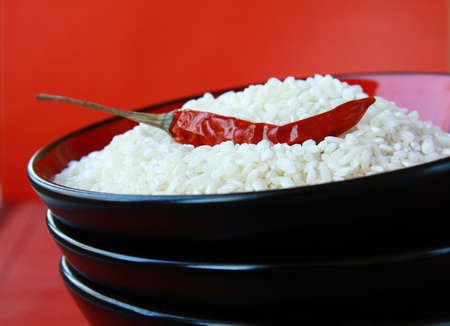 White rice in a black bowl with chili pepper on  red background の写真素材