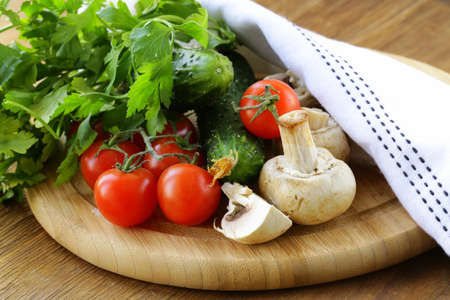 tomatoes, cucumbers, mushrooms and parsley on a cutting boardの写真素材