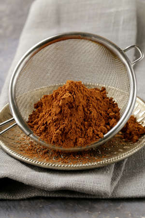 cocoa powder in a metal sieve with a gray backgroundの写真素材