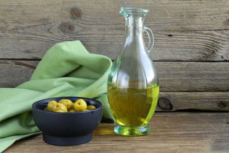 marinated green olives and a bottle of oil on wooden tableの写真素材