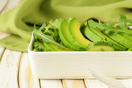 green salad with avocado and arugula in a white bowl
