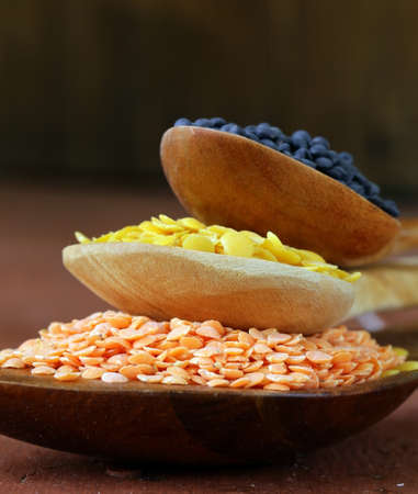 different kinds of lentils - red, yellow and black in wooden spoons