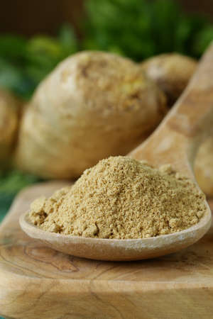 ground ginger in a wooden spoon, fresh root in the background