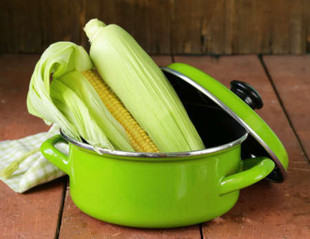 ripe yellow corn and green pan on a wooden backgroundの写真素材