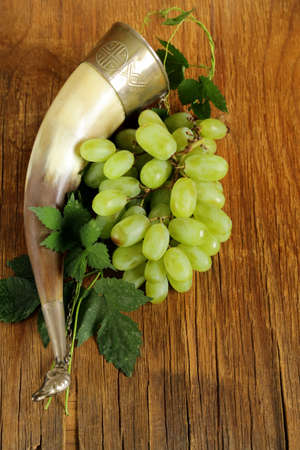 Brush ripe sweet grapes with a traditional drinking horn on wooden backgroundの写真素材
