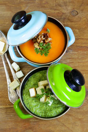 two kinds of cream soup (broccoli and pumpkin) in pot on wooden backgroundの写真素材