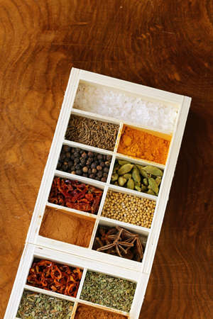 set of different spices (pepper, salt, turmeric, bay leaves, chili, herbs) in a wooden box