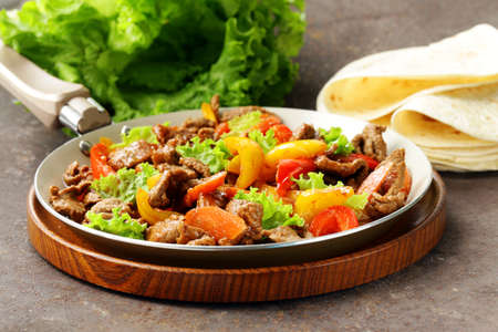 Beef Fajitas with colorful bell peppers in pan on a wooden tableの写真素材