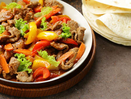 Beef Fajitas with colorful bell peppers in pan on a wooden tableの写真素材
