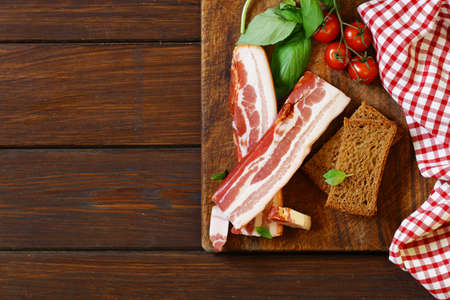 smoked bacon with basil and tomatoes on a cutting boardの写真素材