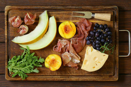 antipasti on a wooden board - prosciutto melone, ham with peaches, cheese and grapesの写真素材