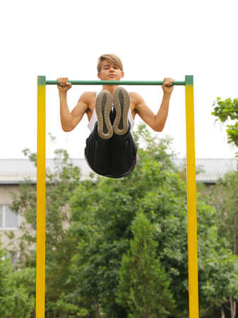 young guy doing exercises on the horizontal bar outdoor (workout)