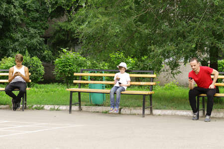 father and two sons sitting on a bench and look at smartphonesの写真素材