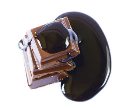 Pieces of dark chocolate and syrup on a white background