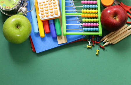 School supplies and apple on a green background