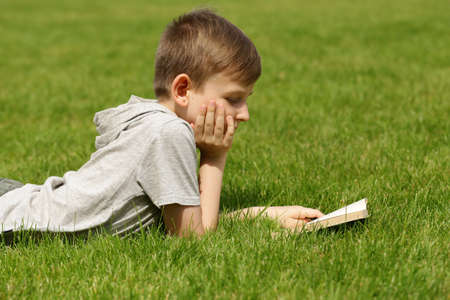 Cute blond boy reading a book in a park outdoorsの写真素材