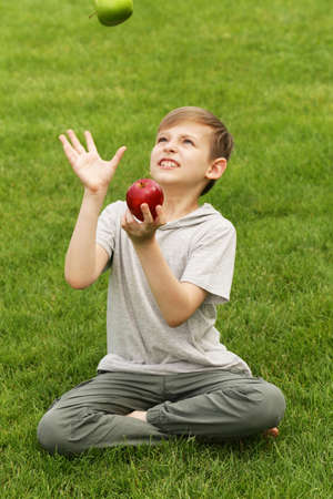 Cute young boy with apples on green grass - summer time, picnicの写真素材