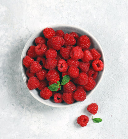 fresh ripe raspberries in a gray plate on a light gray background top view