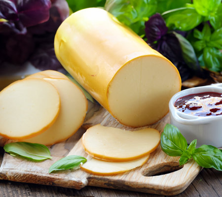smoked cheese on a wooden board with fresh basilの写真素材