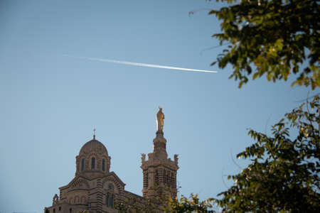 The domes of famous basilicia in the foreground in marseilles. The domes of famous basilicia notre dam de la garde with the golden cross, contrails in the blue skyの写真素材
