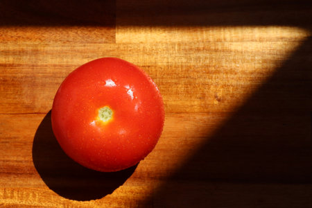 a single tomato on a wooden kitchen chopping boardの写真素材
