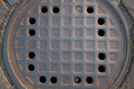 Cast iron manhole cover on cobblestone street in warm light-urban textureの写真素材