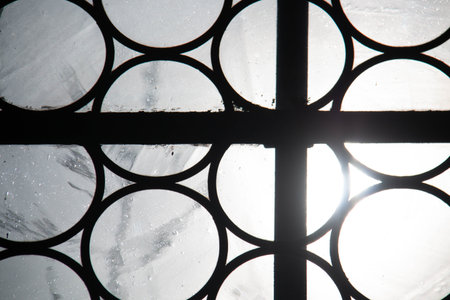 Geometric iron window grille with circular pattern and frosted glass illuminated by sunlight from behindの写真素材