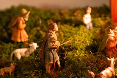 Miniature nativity scene with shepherds, sheep, and moss-covered landscape in soft festive lightingの写真素材