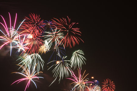 Multiple fireworks explosions in white, pink, and red hues in the night skyの写真素材