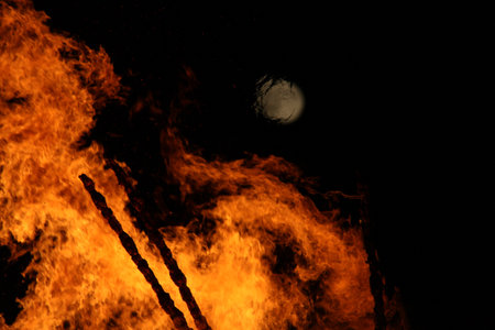 Full moon over a large bonfire with bright orange flames at nightの写真素材