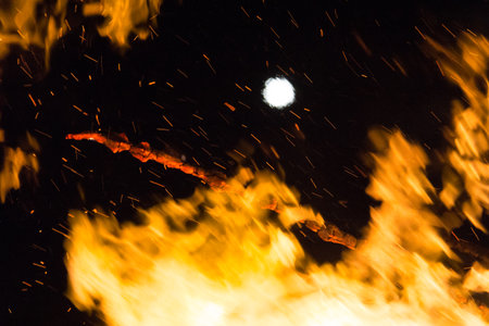 Full moon over a large bonfire with bright orange flames at nightの写真素材